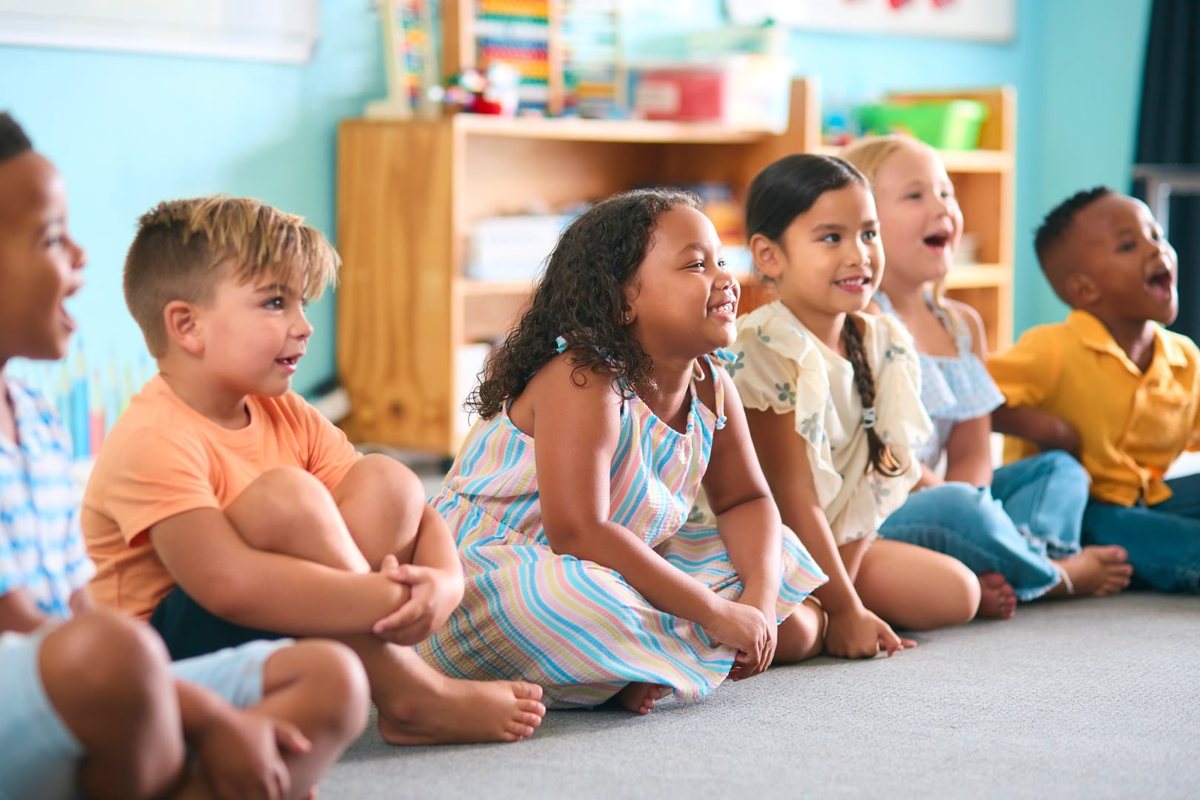 A row of young students sitting on the carpet, caught up in a lesson