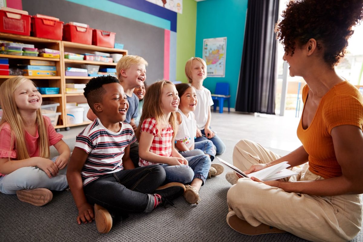 An educator reading aloud to a circle of students sitting on the classroom floor